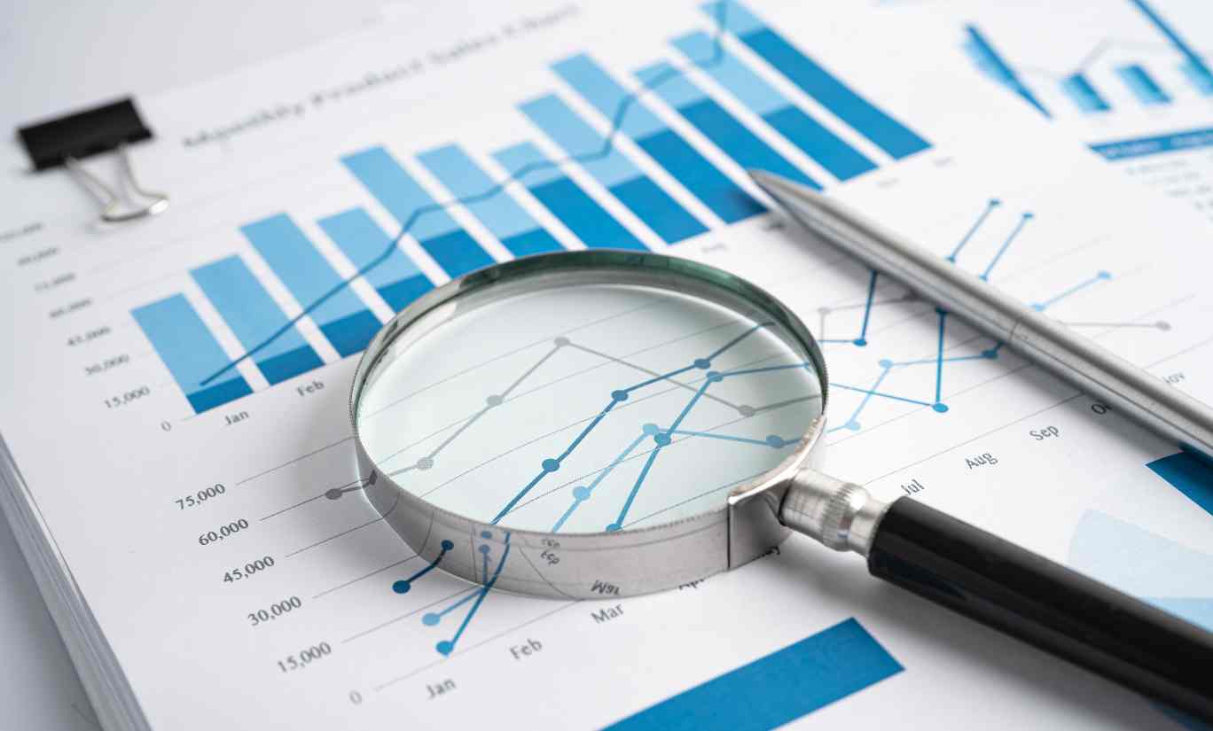 Image of data and a magnifying glass showing an analytics report, Have you Noticed an Increase in Spam Traffic in GA4?