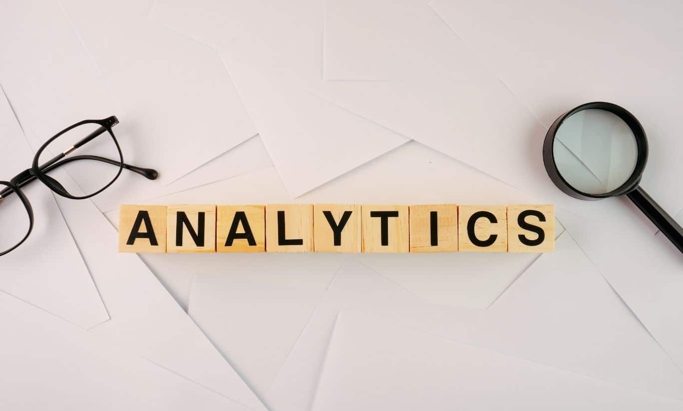 glasses and magnifying glass on top of paper with wooden blocks spelling out analytics