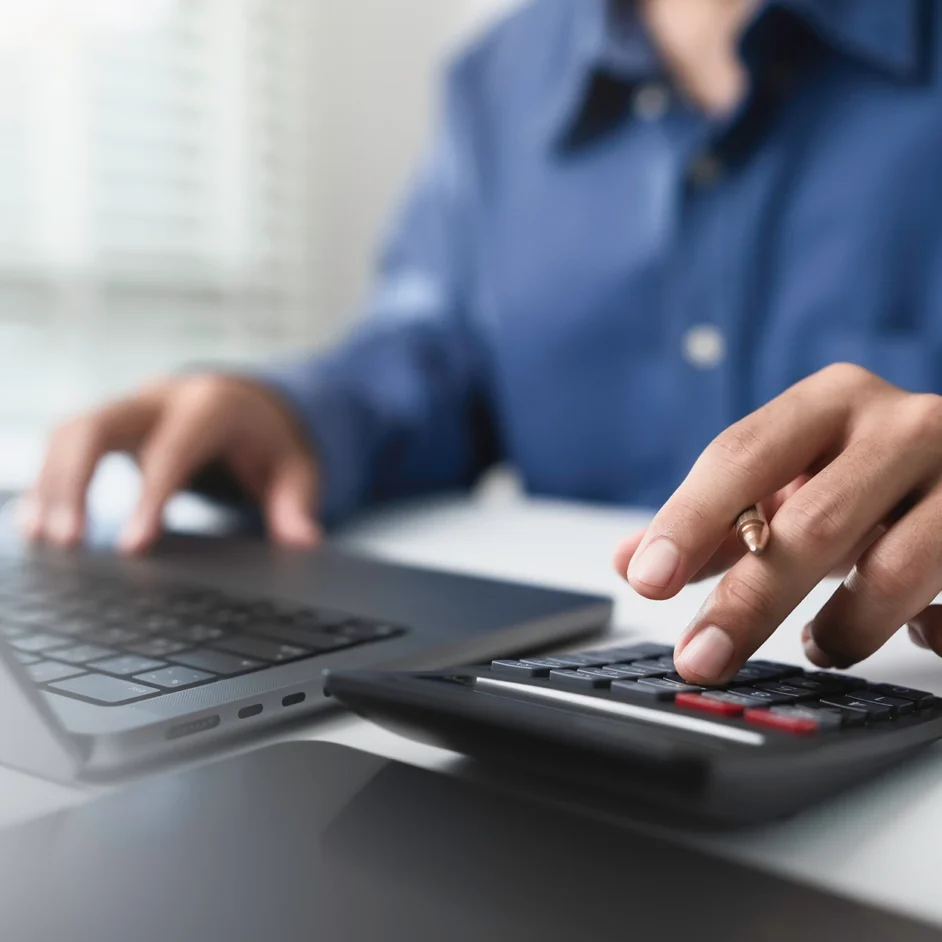 A person calculates on a laptop while using a handheld calculator, focused on their work.