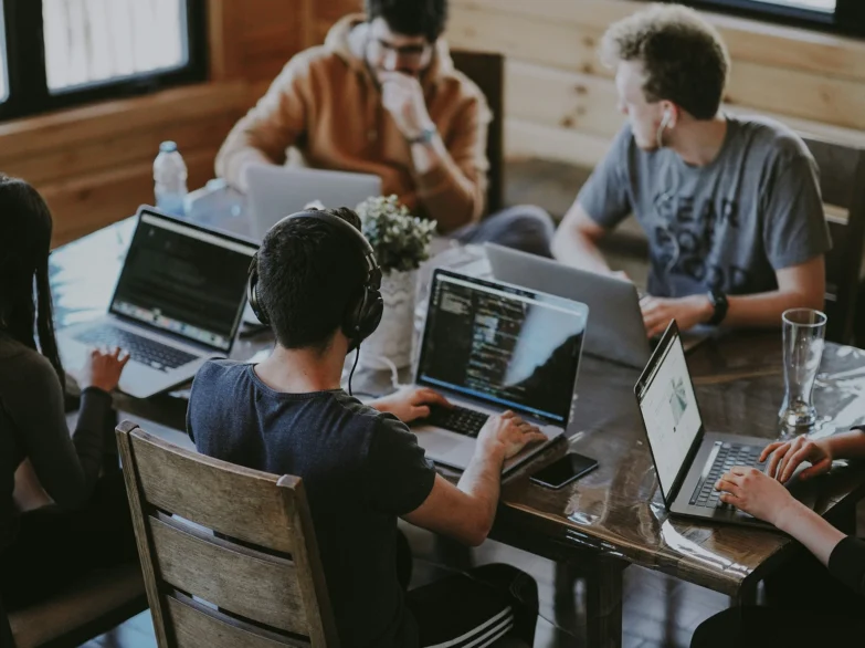 A group of diverse people sitting around a table, each using laptops and engaged in collaboration.