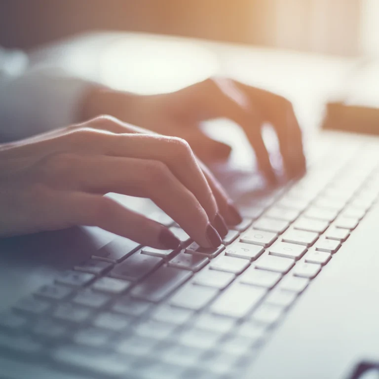 A person focused on typing on a laptop keyboard, with hands positioned over the keys.