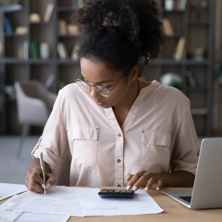 A woman wearing glasses works on her laptop at a desk, focused and engaged in her task.