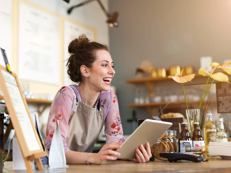 A woman sits at a table, focused on her tablet in her cafe business.
