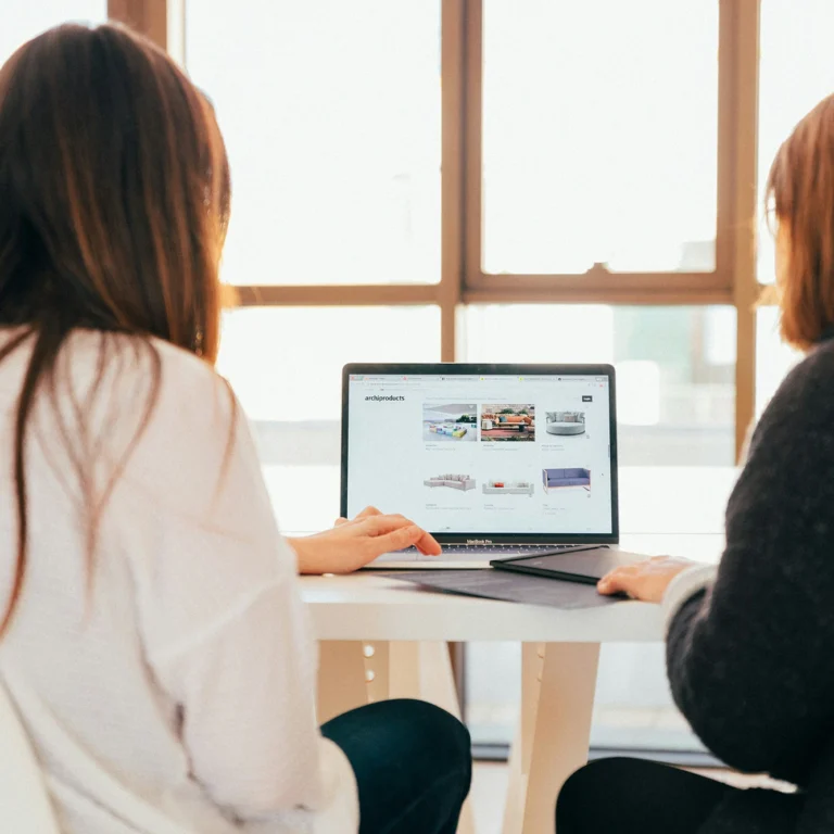 Two women sitting at a table, engaged in conversation while using a laptop.