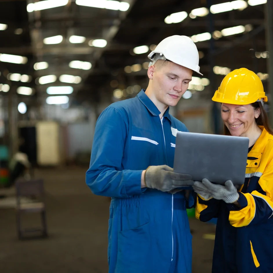 Two people in hard hats collaborating over a laptop, discussing plans or project details.