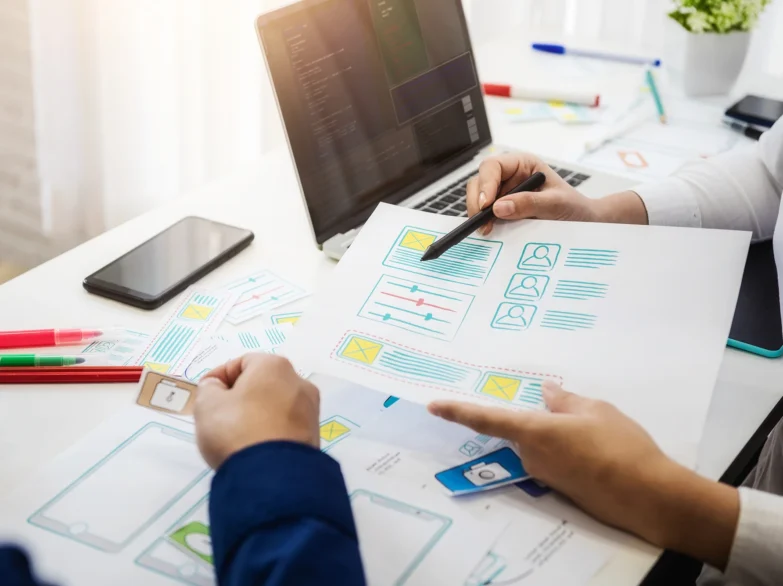 Two people collaborating on a project at a desk, surrounded by papers and a laptop.