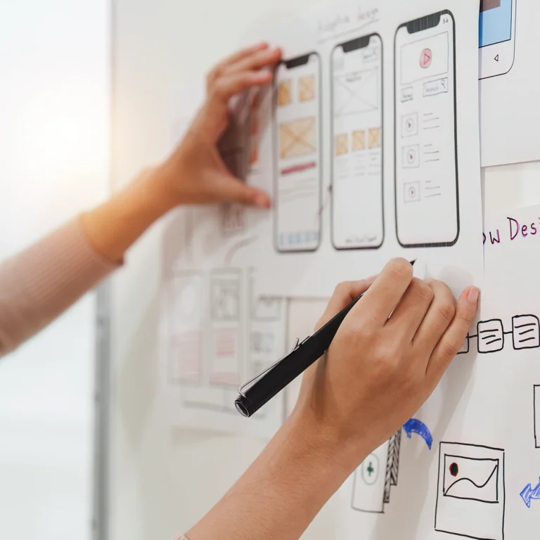 A woman writes on a whiteboard with a pen, focused on her task in a bright, collaborative environment.
