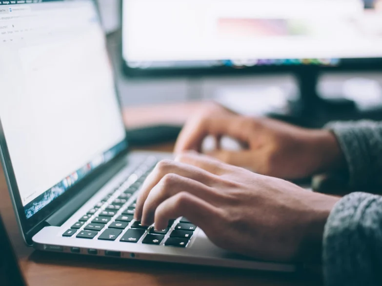 A person typing on a laptop computer, with hands on the keyboard.