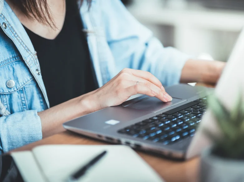 A woman in a blue blouse, focused on typing on a laptop, with her hands on the keyboard.