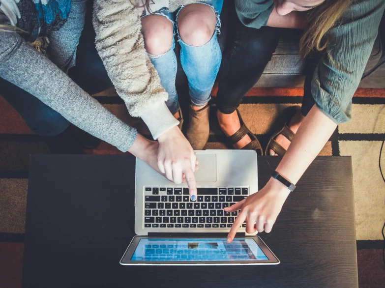 Three women sitting on a couch, looking at a laptop, engaged in a collaborative work session.