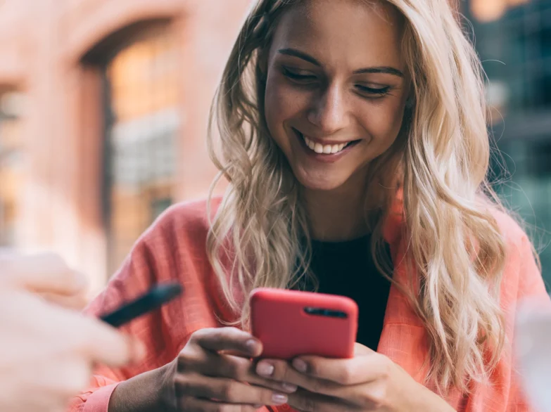 A woman smiles while using her cell phone, enjoying a moment of connection or entertainment.