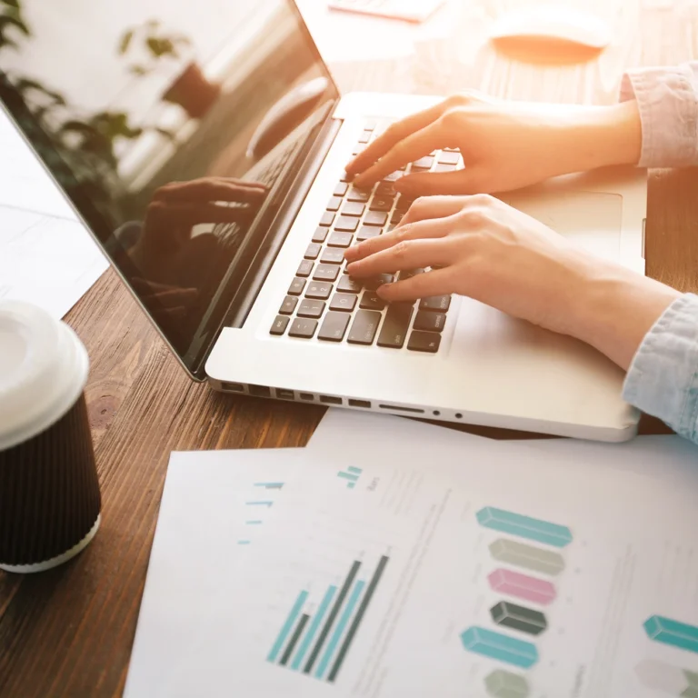 Businesswoman working on a laptop at a desk, surrounded by papers and a cup of coffee.