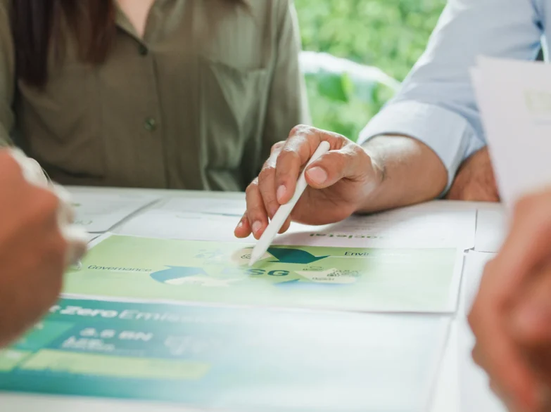 People gathered around a table, reviewing papers and writing with a pen.