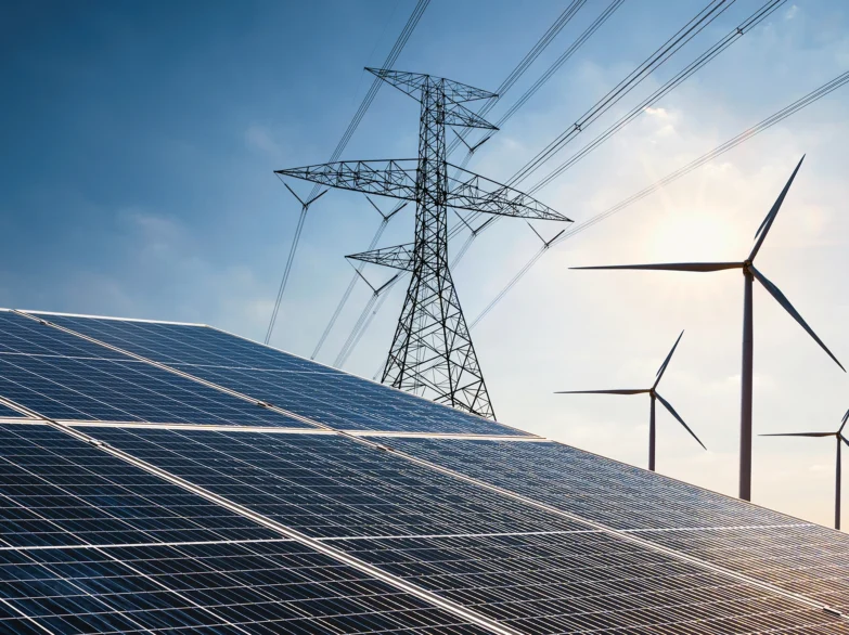 Solar panels in the foreground with wind turbines visible in the background against a clear blue sky.