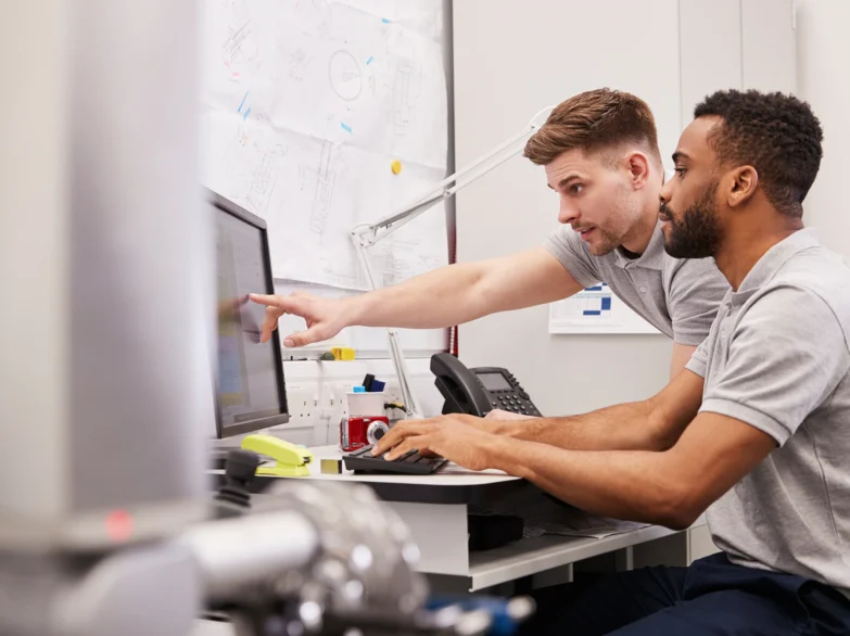 Two men collaborating on a computer in a bright office setting, focused on their work.