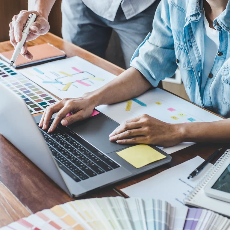 A man and woman collaborate on a laptop, surrounded by colourful swatches for a creative campaign.