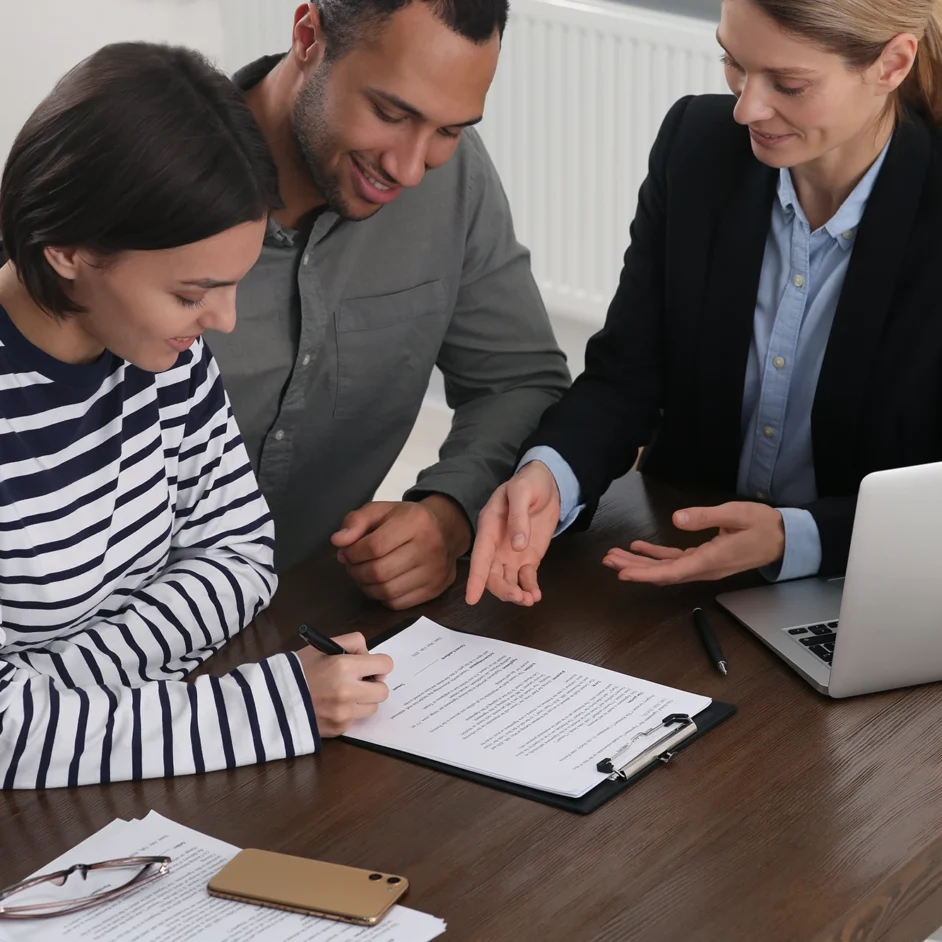 A couple and a man and woman are seated at a table, signing paperwork together.