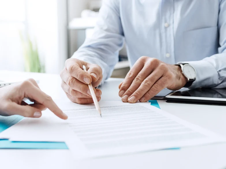 Two people signing documents at a desk, focused on their paperwork in a professional setting.