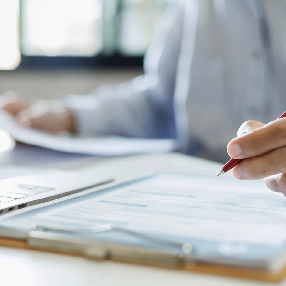A man writes on paper with a pen while using a laptop on a desk.