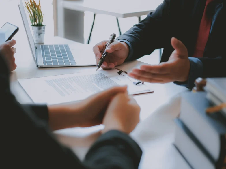 A man and woman sit at a table with a laptop and papers, engaged in discussion.