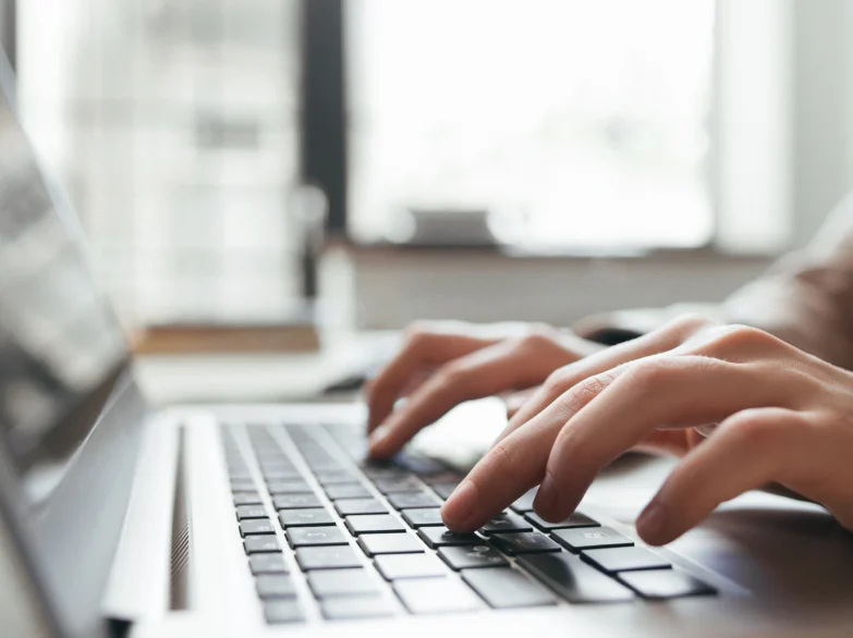 A person focused on typing on a laptop computer, with hands on the keyboard.