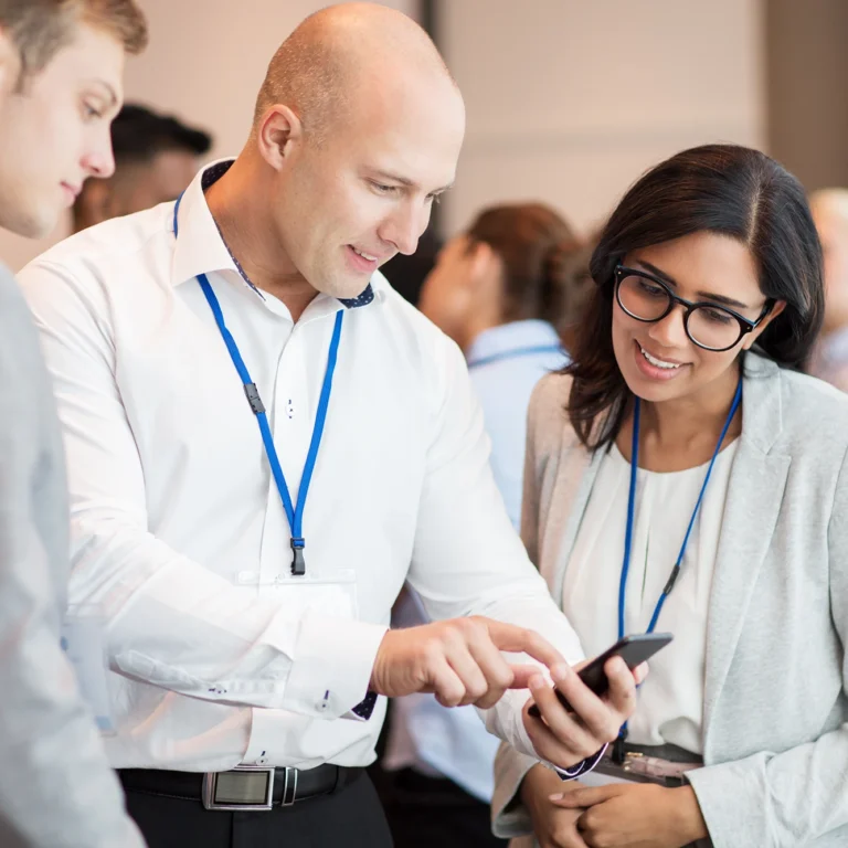 A man and woman are smiling while looking at a cell phone together, sharing a moment of connection.