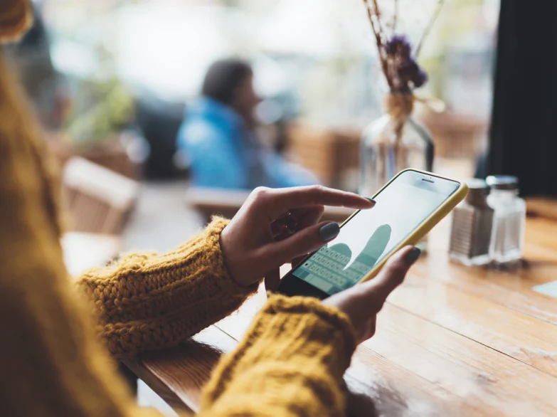 A woman sitting in a cafe, focused on her smartphone while enjoying her drink.