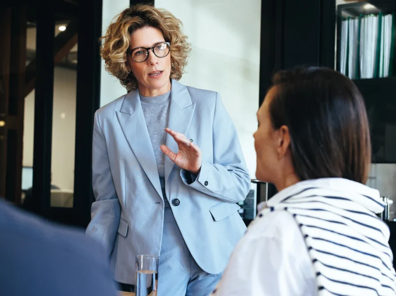A woman in a business suit engages in conversation with a group of people in a professional setting.