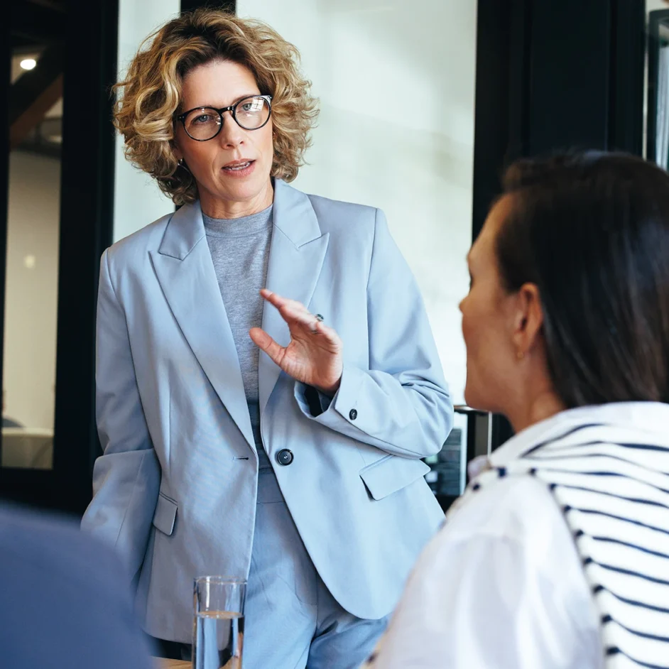 A woman in a business suit engages in conversation with a group of people in a professional setting.