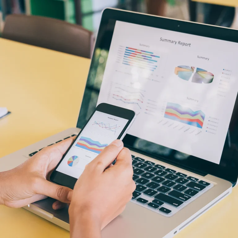 A person using a smartphone and laptop while sitting at a desk, focused on their work.