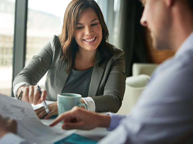 A woman and man sit at a table, reviewing paperwork together with focused expressions.