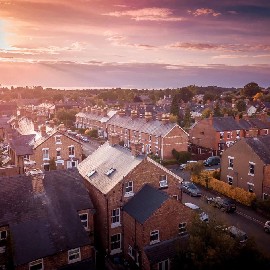 Aerial view of a residential area bathed in warm sunset hues, showcasing rooftops and streets below.