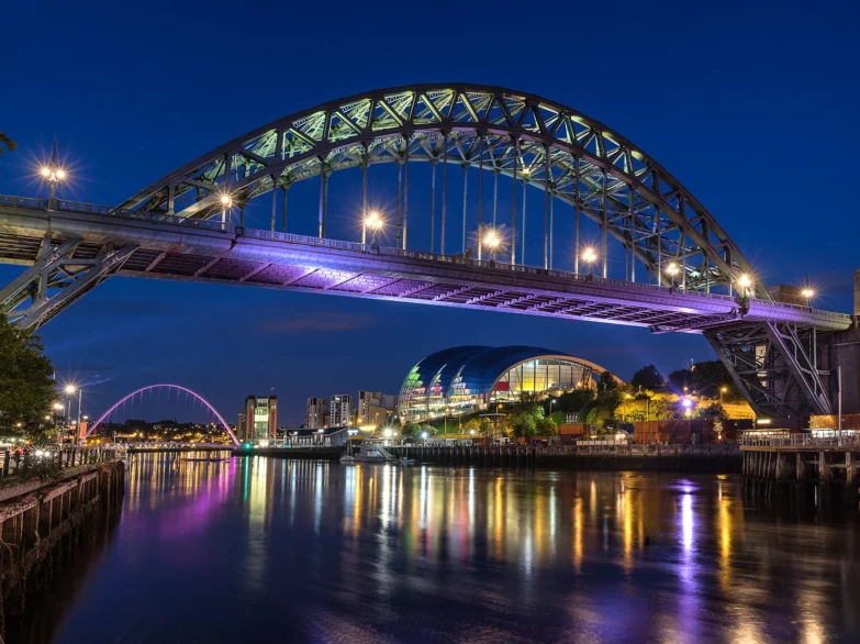 Newcastle and Gateshead Quayside at night, reflecting shimmering lights on the River Tyne's surface.
