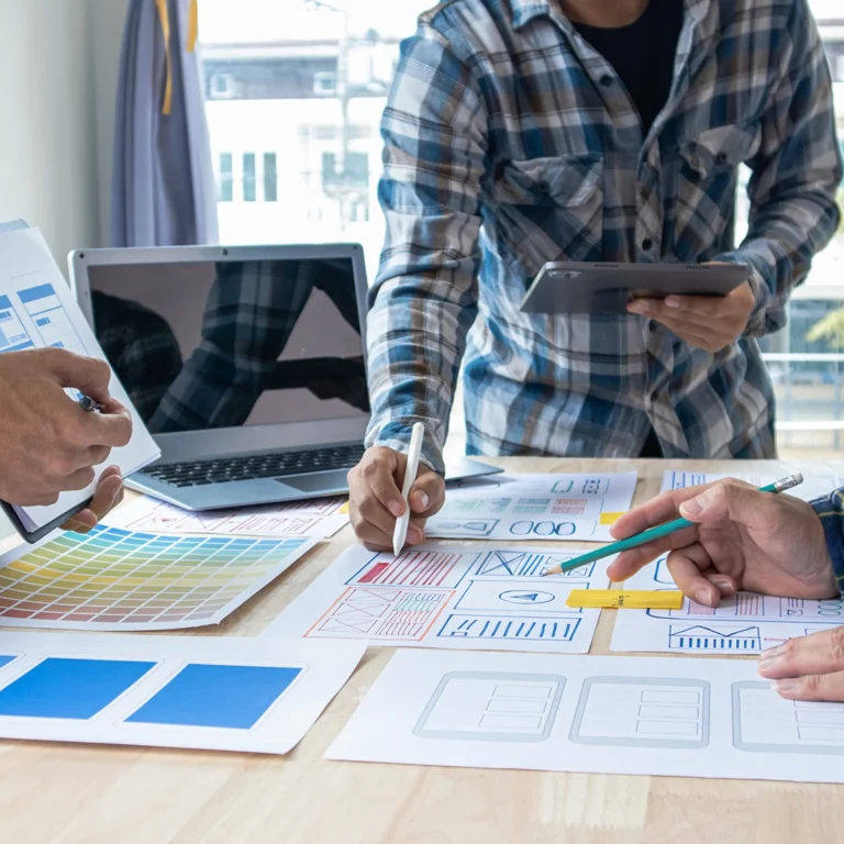 Three people collaborating on a design project, discussing ideas and reviewing sketches at a table.