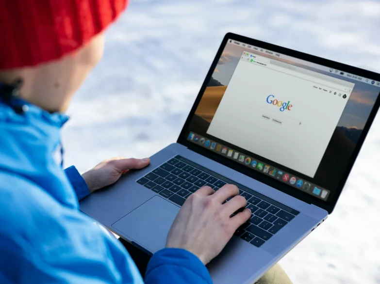 Woman in a red hat, using a laptop to search Google against a snowy backdrop.