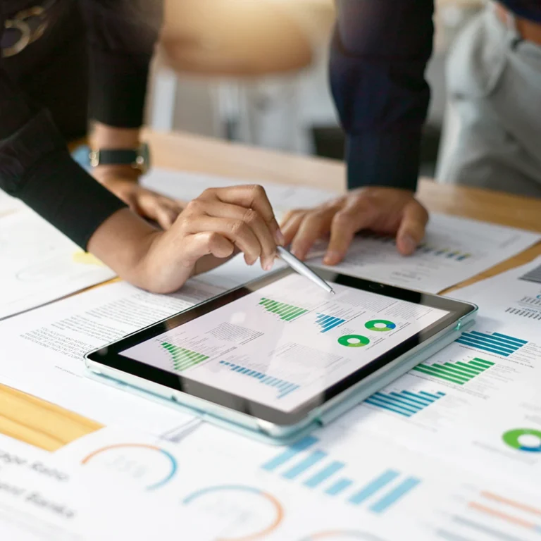 Business professionals collaborating on a tablet, surrounded by papers and graphs for analysis and planning.
