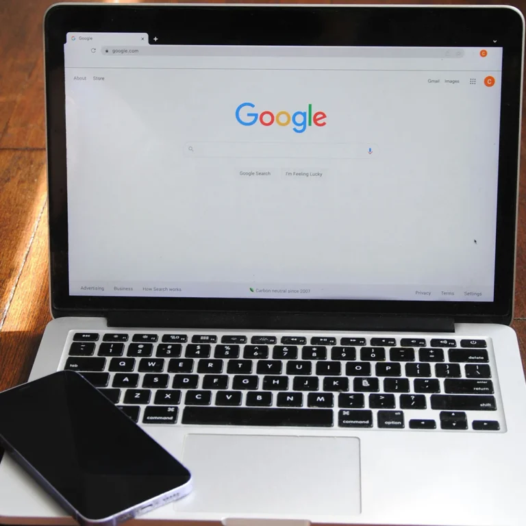 A MacBook laptop with Google search engine on the screen and a smartphone.