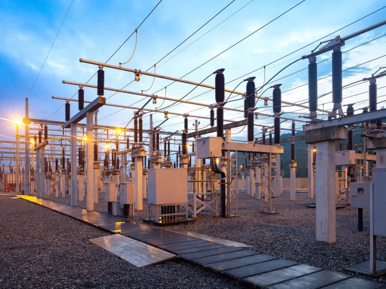 A large electrical substation featuring numerous wires and tall poles against a clear sky.