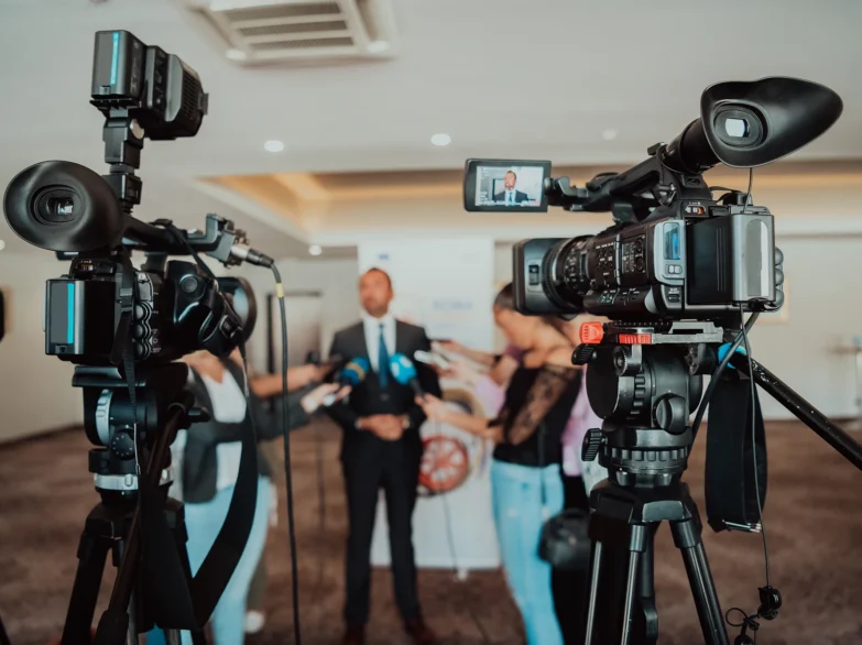 A man in a suit stands confidently in front of a camera, ready to speak.