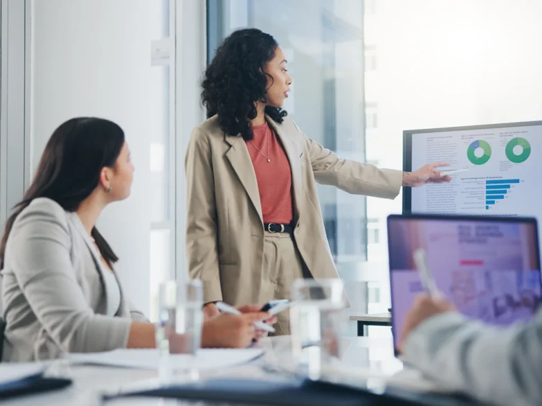 A woman presents to her colleagues in a bright conference room, engaging them with her ideas and visuals.