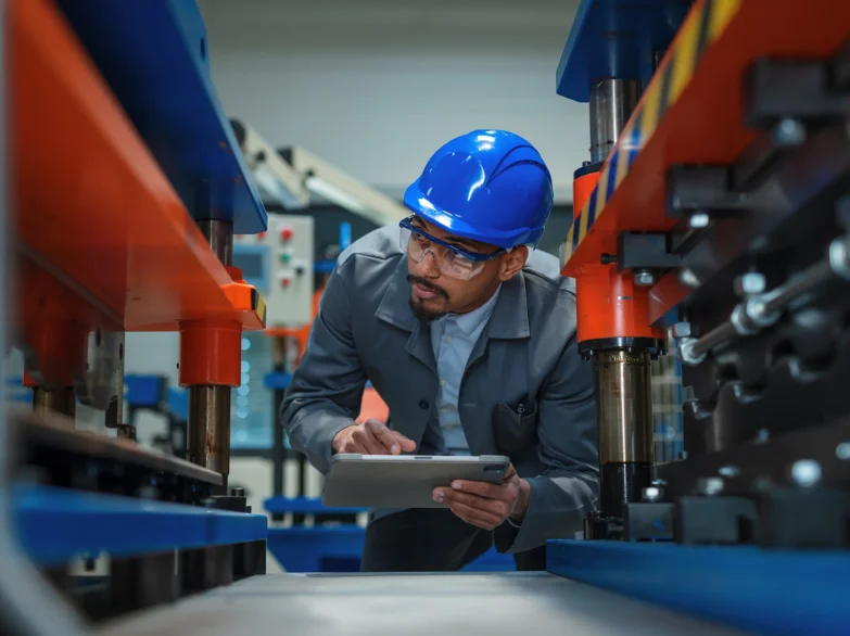 A man wearing a hard hat and glasses is focused on using a tablet.