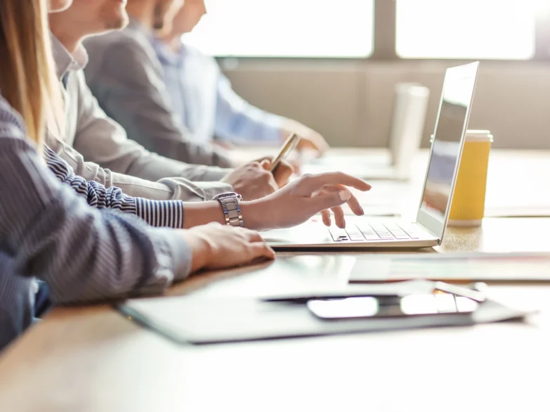 People collaborating at a table, using laptops and reviewing papers during a productive meeting.