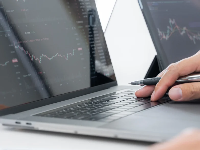 A person analyses graphs on a laptop while taking notes with a pen.