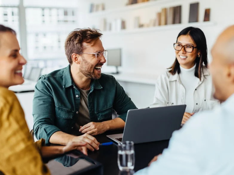 Four people engaged in discussion around a table with a laptop open in front of them.