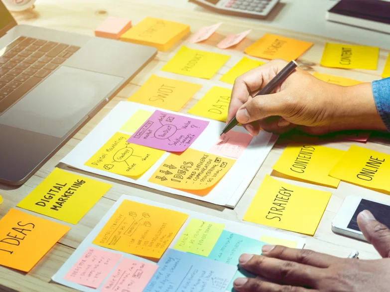A person writes on paper surrounded by colourful sticky notes.