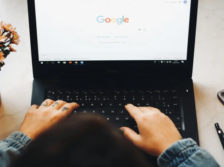 Woman typing on a laptop keyboard with Google search on the screen.