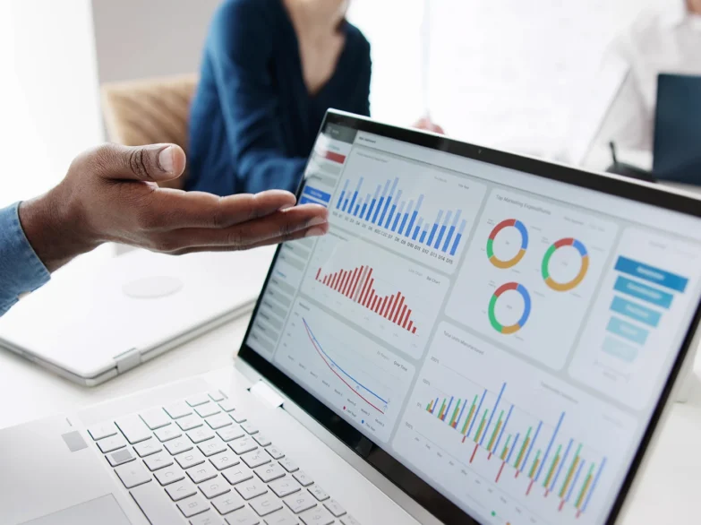 A person points at a laptop screen displaying colourful graphs and data visualisations.
