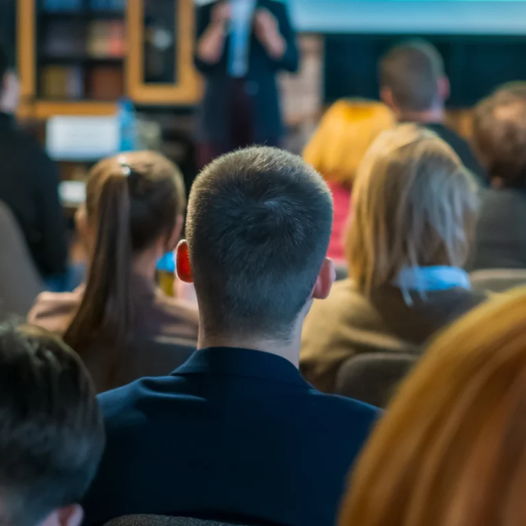 A diverse group of people engaged in discussion while seated around a conference table in a well-lit room.