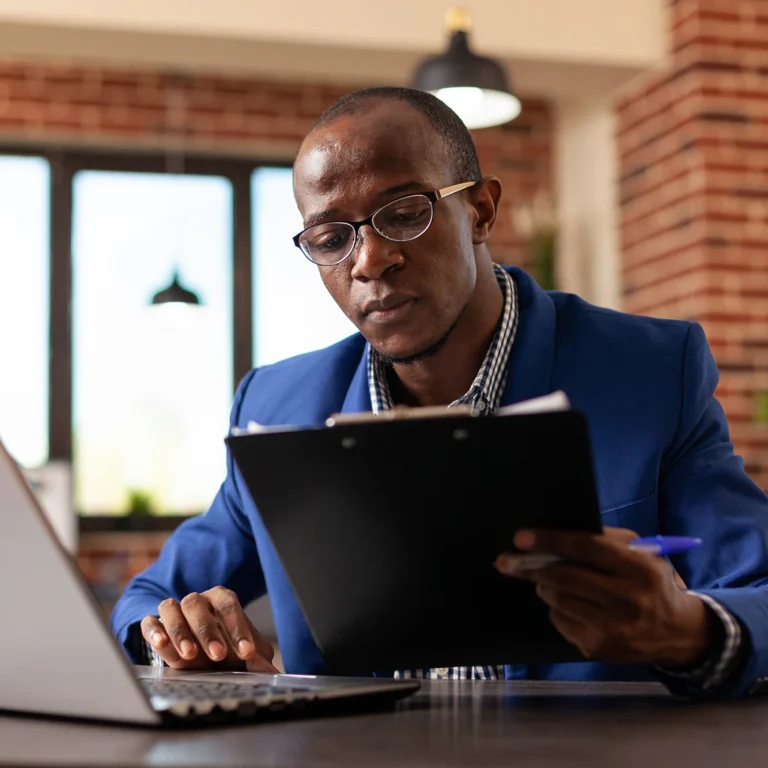 A man in a suit is focused on his laptop, working intently in a modern office setting.