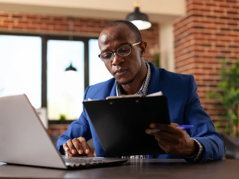 A man in a suit is focused on his laptop, working intently in a modern office setting.
